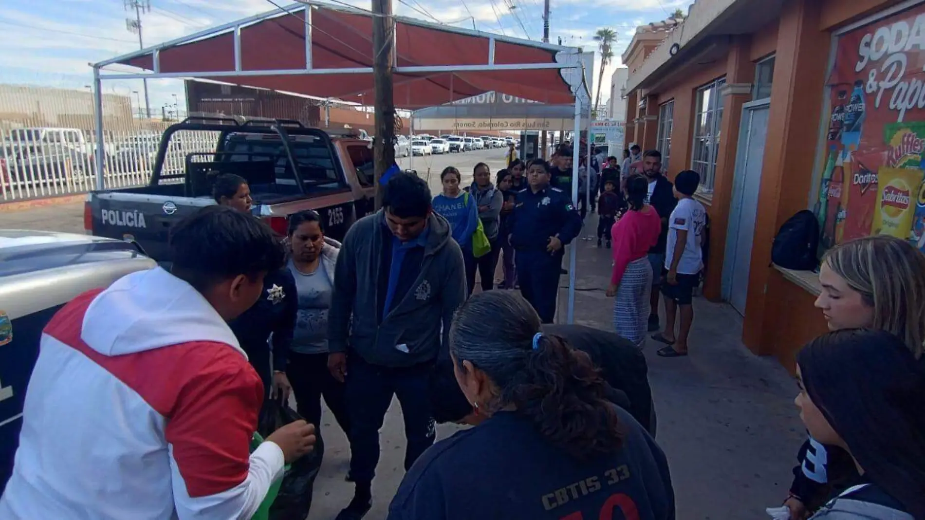 Alumnos del CBTIS33 y policías municipales proporcionaron alimentos y artículos de higiene a migrantes que esperan cita para solicitar asilo, frente a la aduana de los Estados Unidos.